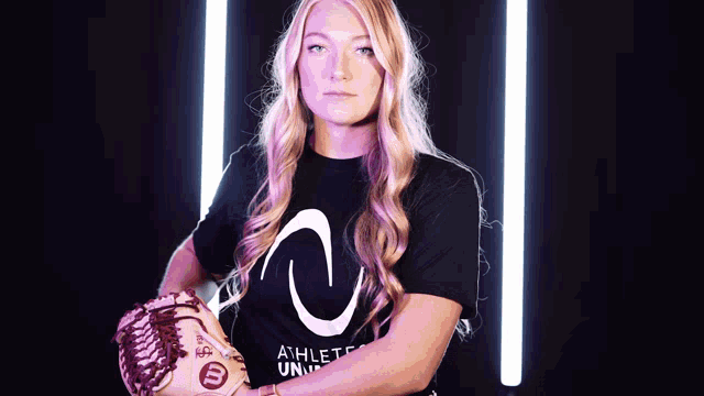 a woman wearing an athletes university shirt holds a baseball mitt