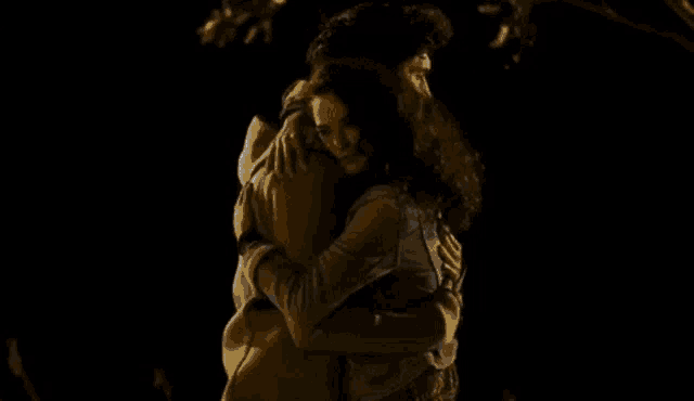 a man and a woman are hugging each other in the dark with a heart in the corner .