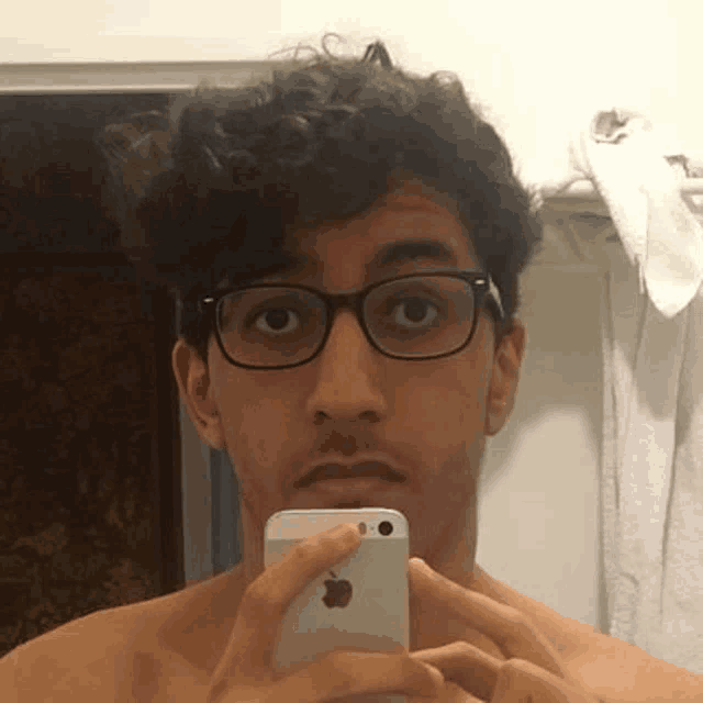 a young man wearing glasses is taking a selfie with his cell phone in a bathroom .