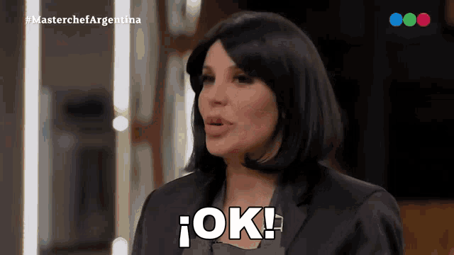 a woman in a black suit says ok in spanish