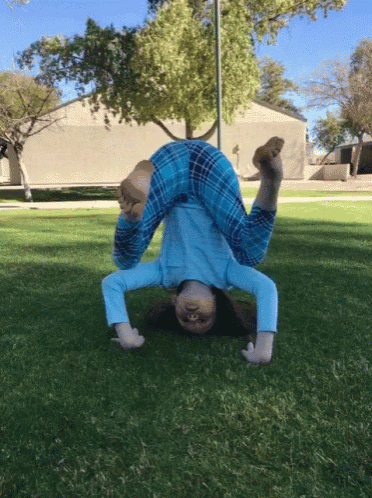 a little girl in blue pajamas is doing a handstand in the grass