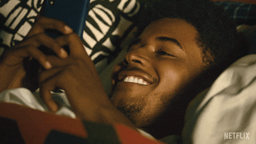 a man is laying in bed looking at his phone with a netflix logo on the bottom right