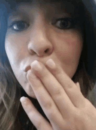 a woman is covering her mouth with her hand and making a funny face .