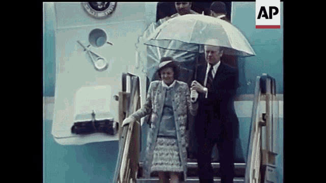 a man holds an umbrella over a woman who is walking down the stairs of a plane