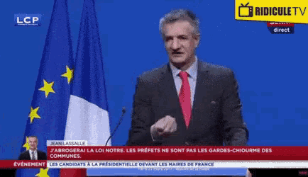 a man in a suit and tie is giving a speech in front of a french flag ..