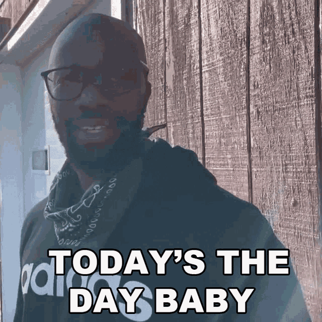 a man wearing glasses and a bandana is standing in front of a wooden wall and says today 's the day baby