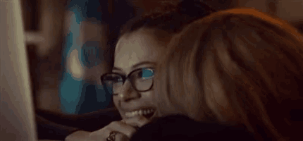 a woman wearing glasses is kissing another woman on the cheek .