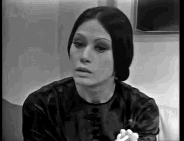 a black and white photo of a woman smoking a cigarette and looking at the camera .