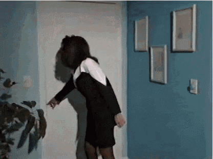 a woman in a black dress is standing in a room with a blue wall .