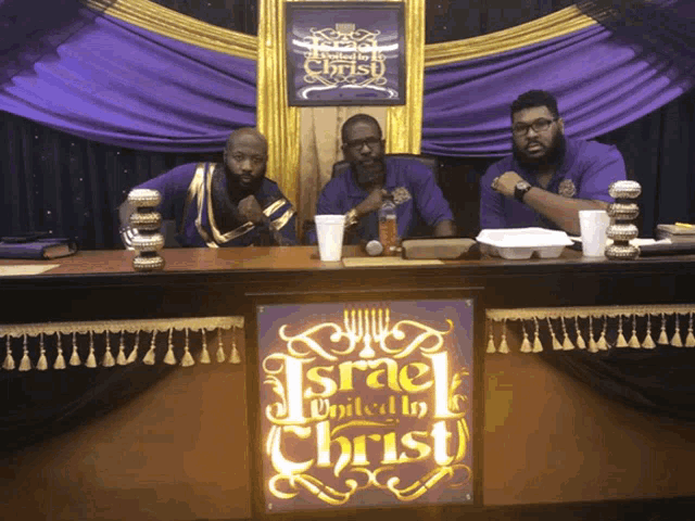 three men sitting at a table in front of a sign that says israel united to christ