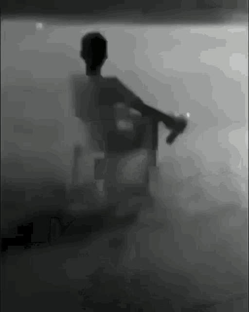 a black and white photo of a person sitting on a chair in a foggy room .