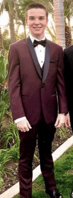 a man in a burgundy tuxedo and bow tie is standing next to a man in a black tuxedo .