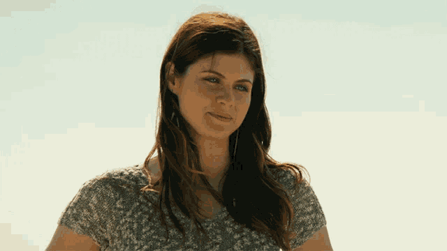 a woman wearing a gray shirt looks at the camera