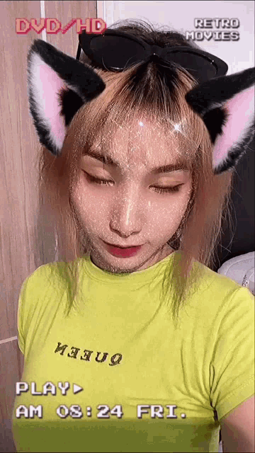 a woman wearing cat ears and a yellow shirt says play am 08 24 fri
