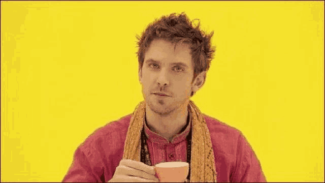 a man in a red shirt and scarf is drinking from a cup on a yellow background .