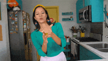 a woman giving a thumbs up in a kitchen with the word coquette on the wall