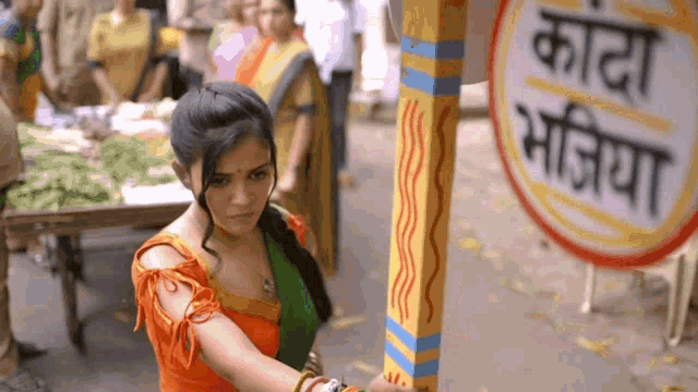 a woman in an orange top stands in front of a sign that says ' kada mojiya ' on it