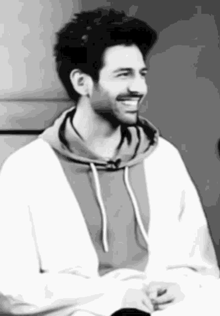 a black and white photo of a man wearing a hoodie and smiling