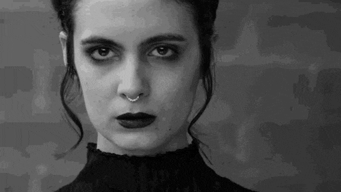 a black and white photo of a woman wearing a nose ring and black lipstick .