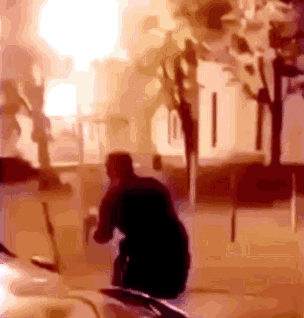 a man is kneeling down in front of a building with a fire in the background .