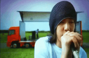 a man in a beanie is singing into a microphone in front of a truck