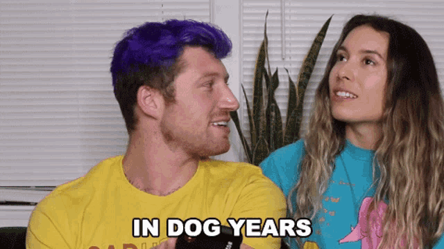 a man with purple hair is talking to a woman who is wearing a blue shirt