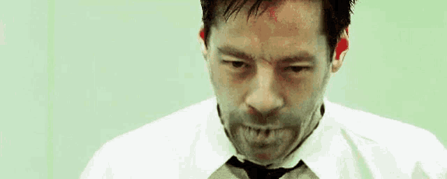 a man in a white shirt and tie with blood on his face is looking down .