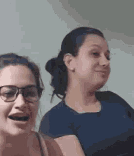 two women wearing glasses and a blue shirt are standing next to each other .
