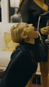a woman is drinking from a glass while another woman holds a wine glass