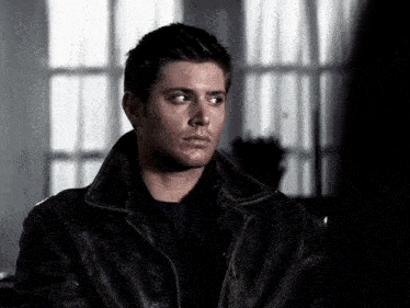 a man wearing a black leather jacket looks to the side