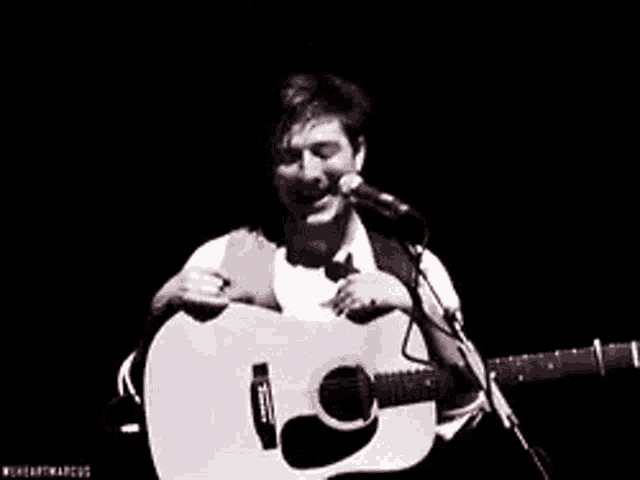 a man is holding a guitar and singing into a microphone while laughing .