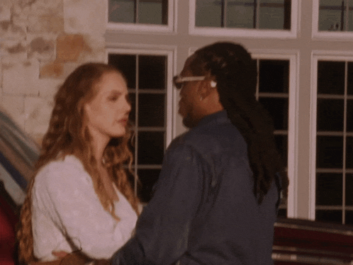 a man and a woman are standing next to each other in front of a window