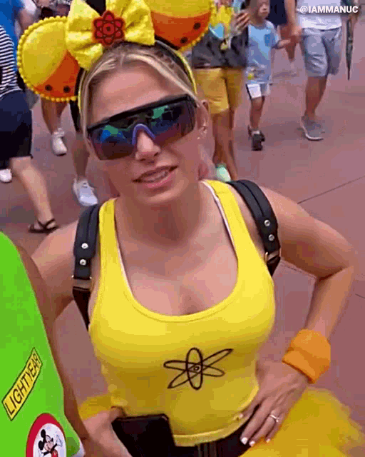a woman wearing sunglasses and a yellow tank top with an atom embroidered on it