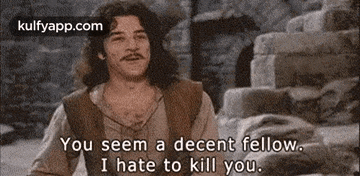a man with long hair and a mustache is talking to another man in a movie .