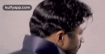 a man with curly hair is standing in front of a white wall and looking down .