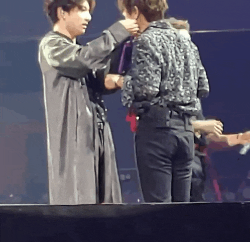 two men are standing next to each other on a stage and one of them is holding another man 's hand .