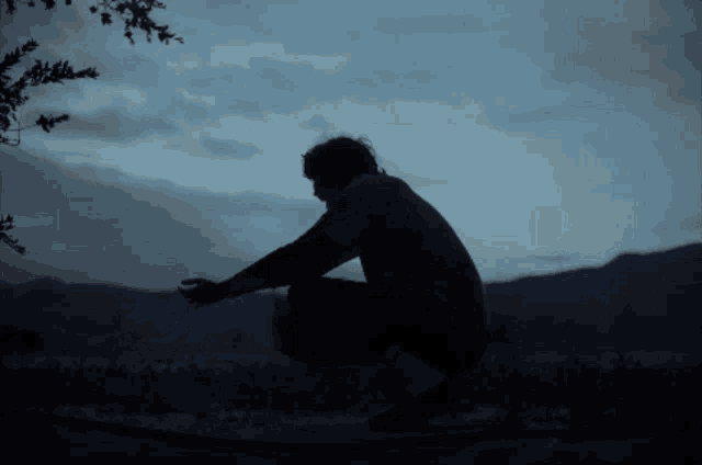 a silhouette of a man squatting down with mountains in the background