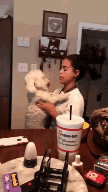 a girl holding a poodle next to a cup that says cook-out creamery