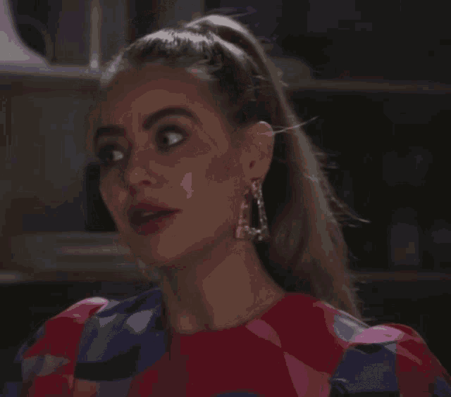 a woman wearing a ponytail and earrings looks at the camera with a serious look on her face
