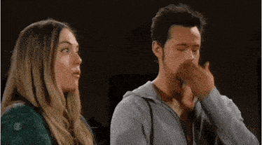 a man and a woman are standing next to each other with the man covering his nose with his hand .