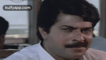 a man with a mustache and a white shirt is sitting at a table looking at the camera .
