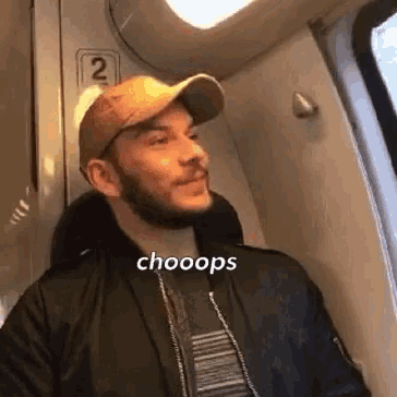 a man with a beard is sitting on a train wearing a baseball cap and a jacket .
