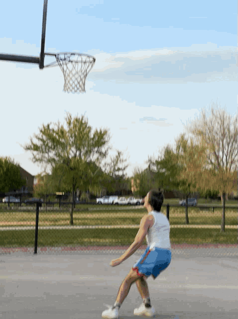 a man in a white tank top and blue shorts is playing basketball on a court