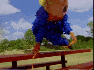 a person in a blue costume is jumping over a red picnic table
