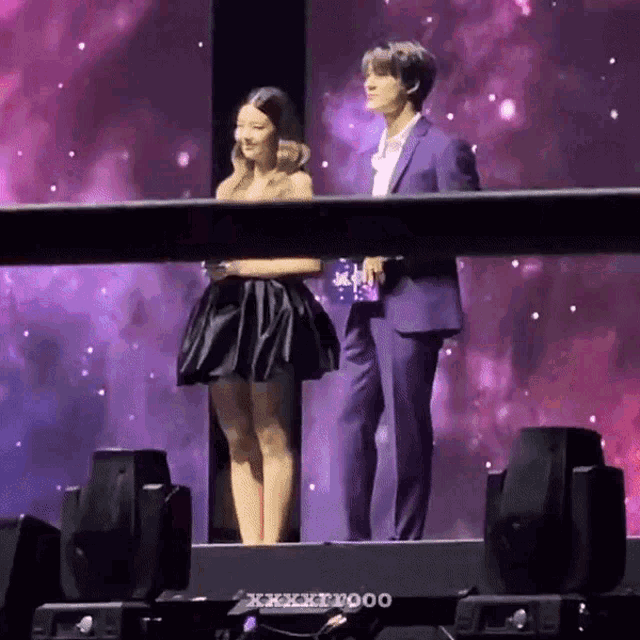 a man in a suit stands next to a woman in a black dress on a stage .