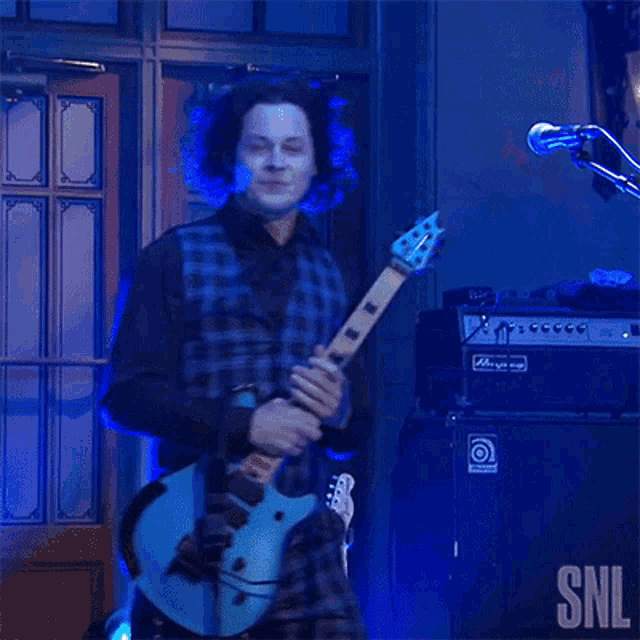 a man playing a guitar in front of a microphone with snl written on the bottom