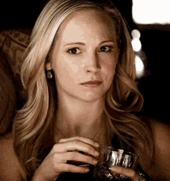 a woman is holding a glass of wine in her hand and looking at the camera .