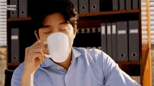 a man in a blue shirt is drinking from a white cup .