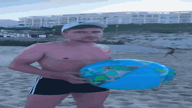 a shirtless man is holding a large inflatable globe on the beach