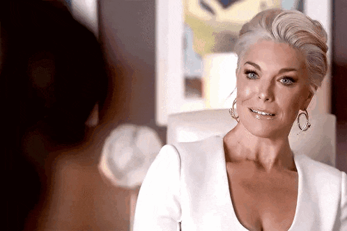 a woman in a white dress and earrings is sitting in a chair .